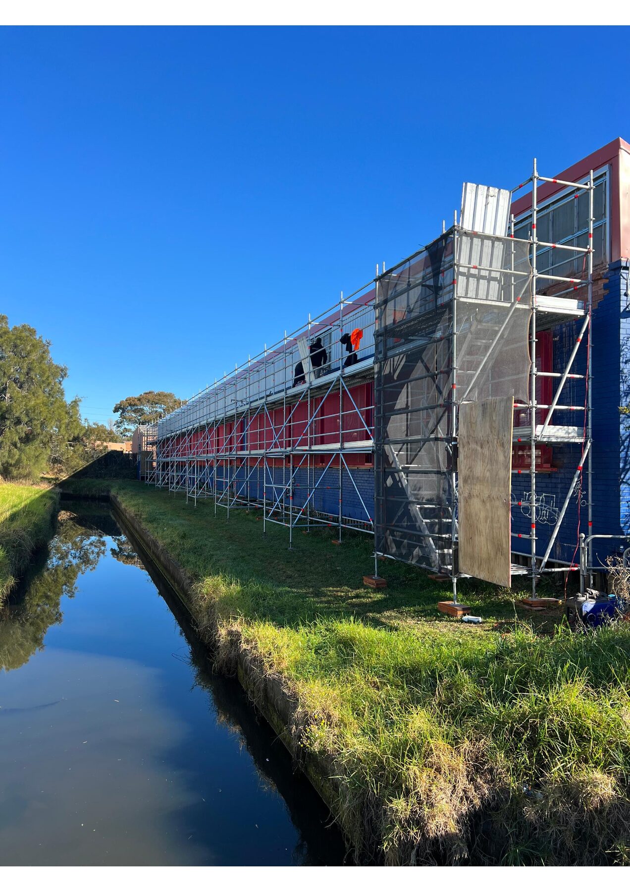 Long industrial Vinnies building with full-length scaffolding alongside a canal at Wollongong